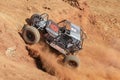 Blue Car powering up steep hill, kicking up sand and dust.